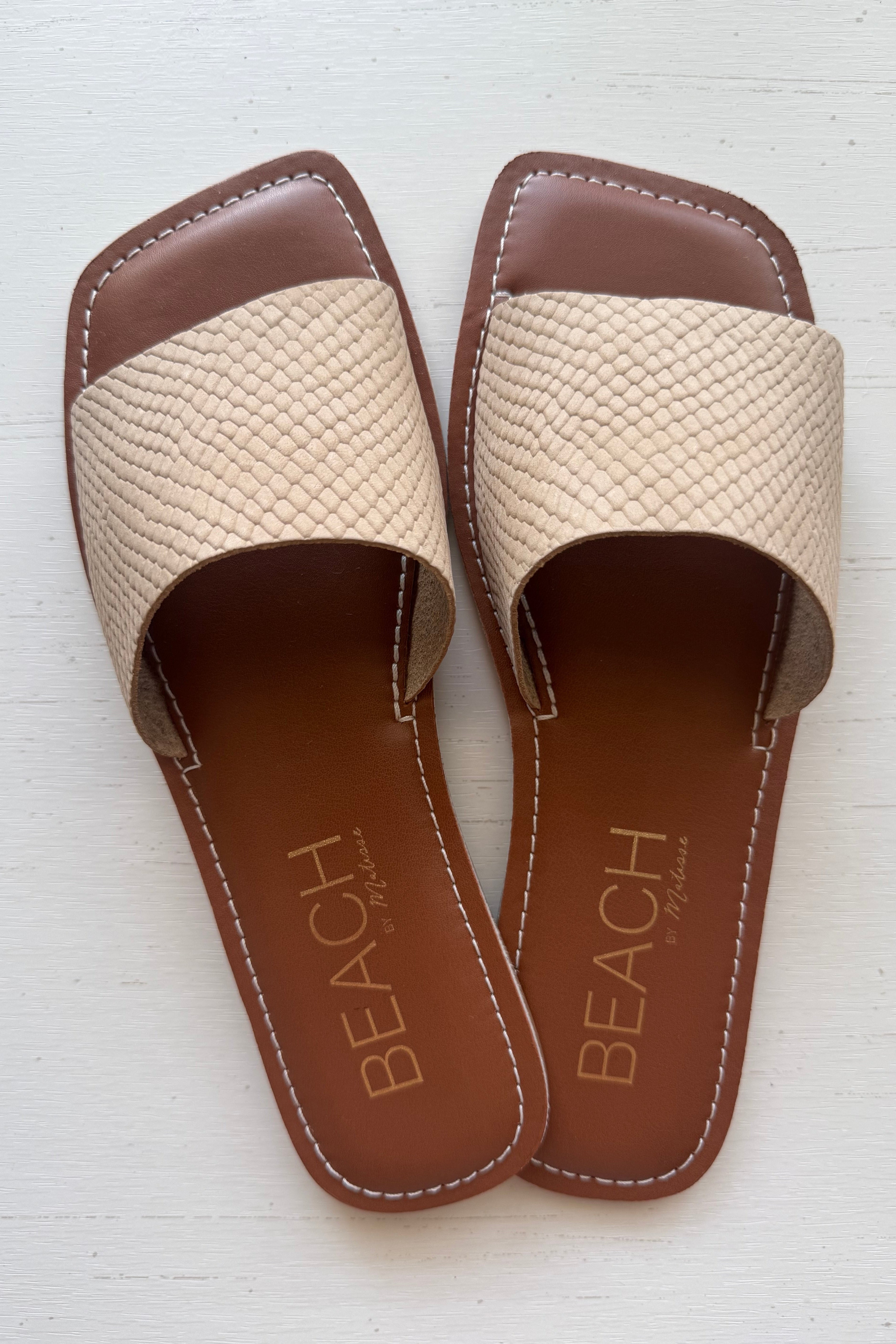 Pair of beige sandals with brown soles on a white background