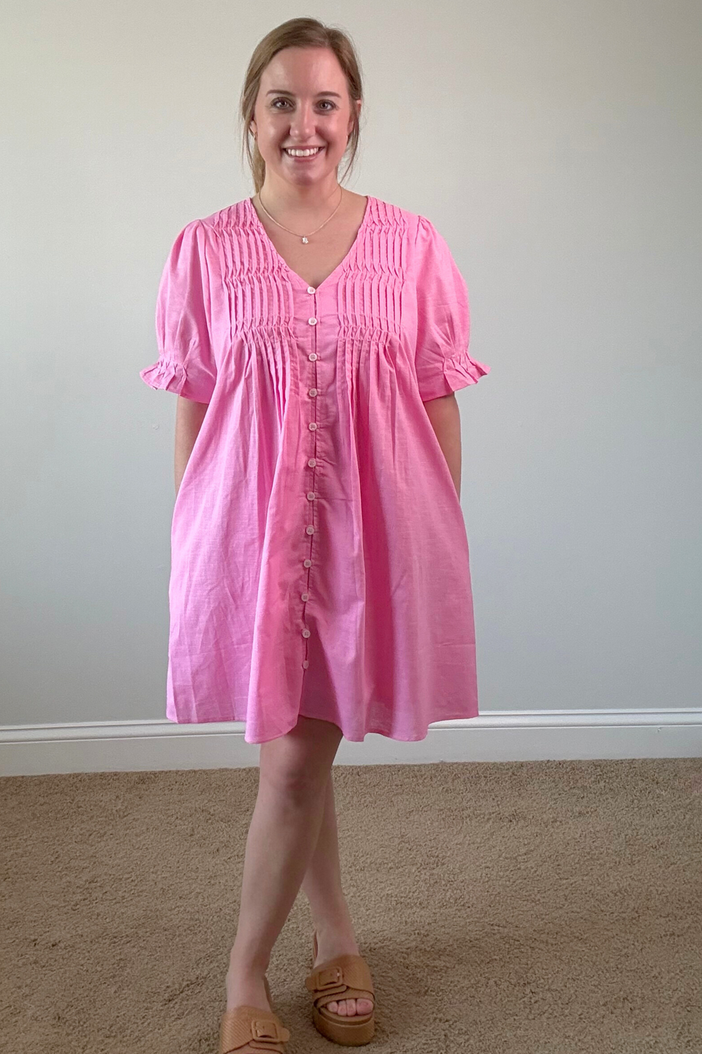 Woman wearing a pink dress standing against a plain wall.