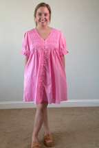 Woman wearing a pink dress standing against a plain wall.