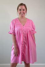 Woman wearing a pink dress standing against a plain wall.