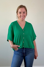 Woman wearing a green blouse and blue jeans against a plain background