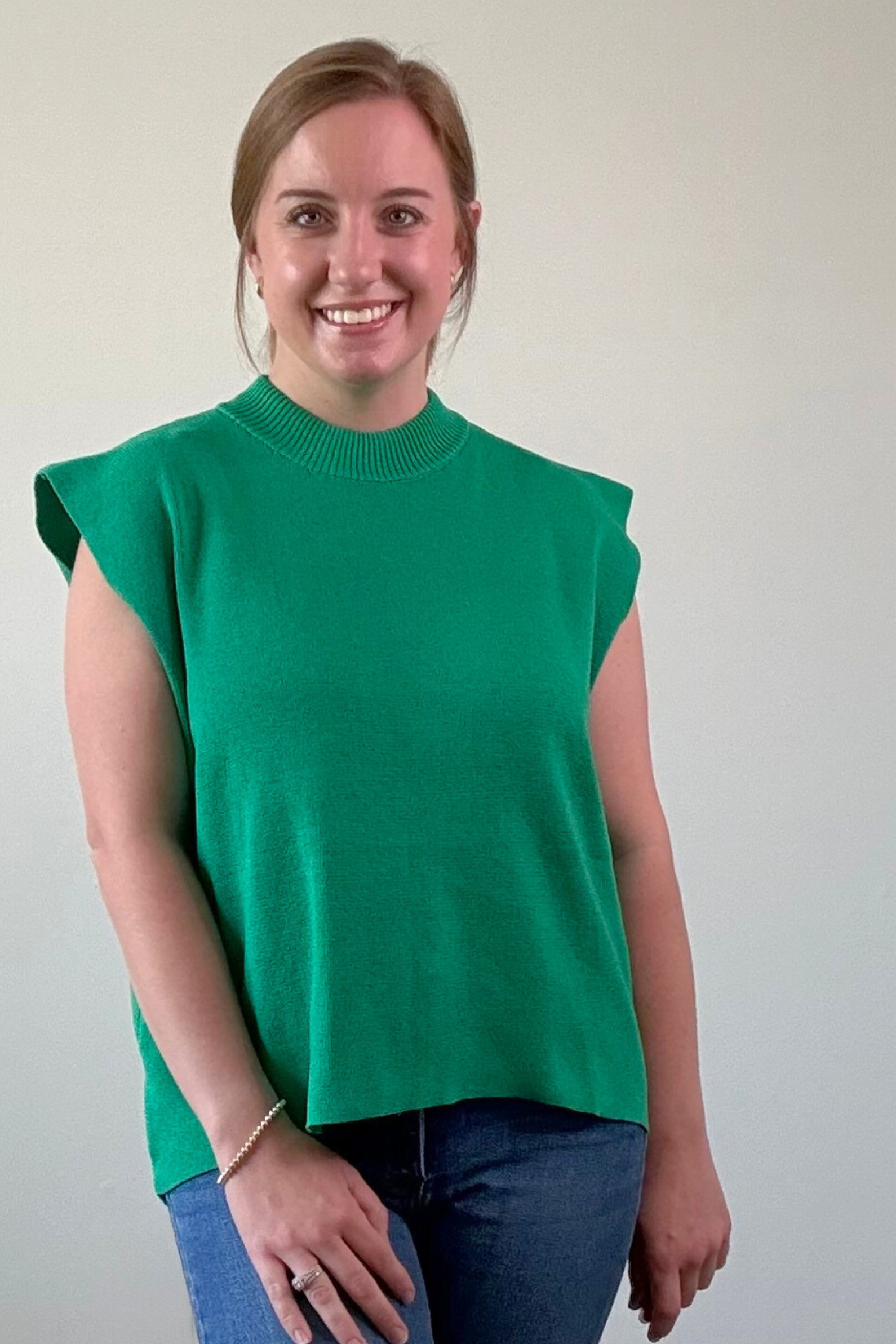 Woman wearing a green sleeveless sweater against a plain background