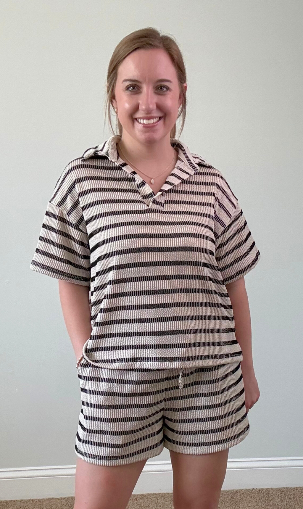 Woman wearing a striped outfit against a plain wall.