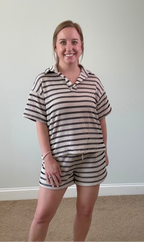 Woman wearing a striped outfit standing against a plain wall.