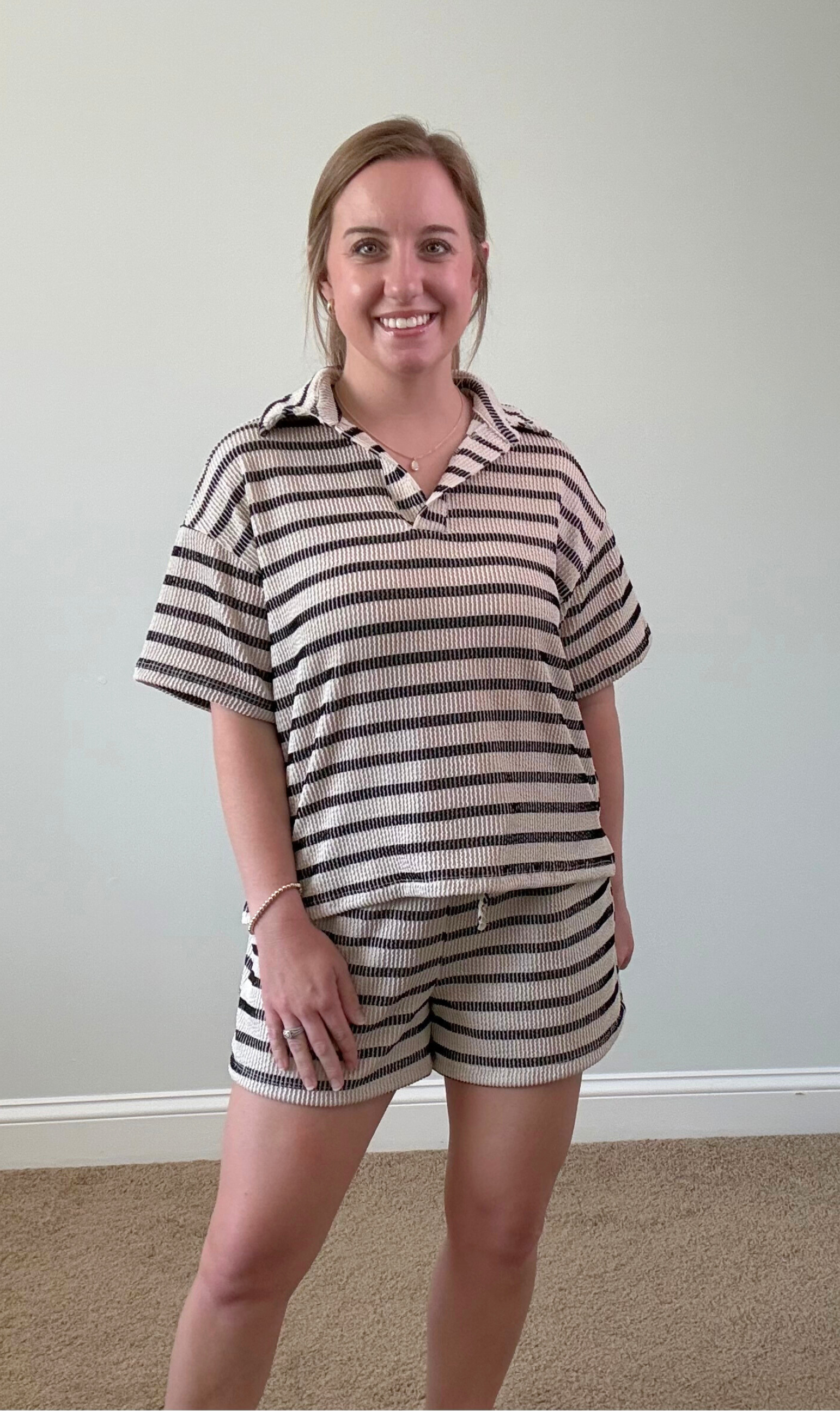 Woman wearing a striped outfit standing against a plain wall.