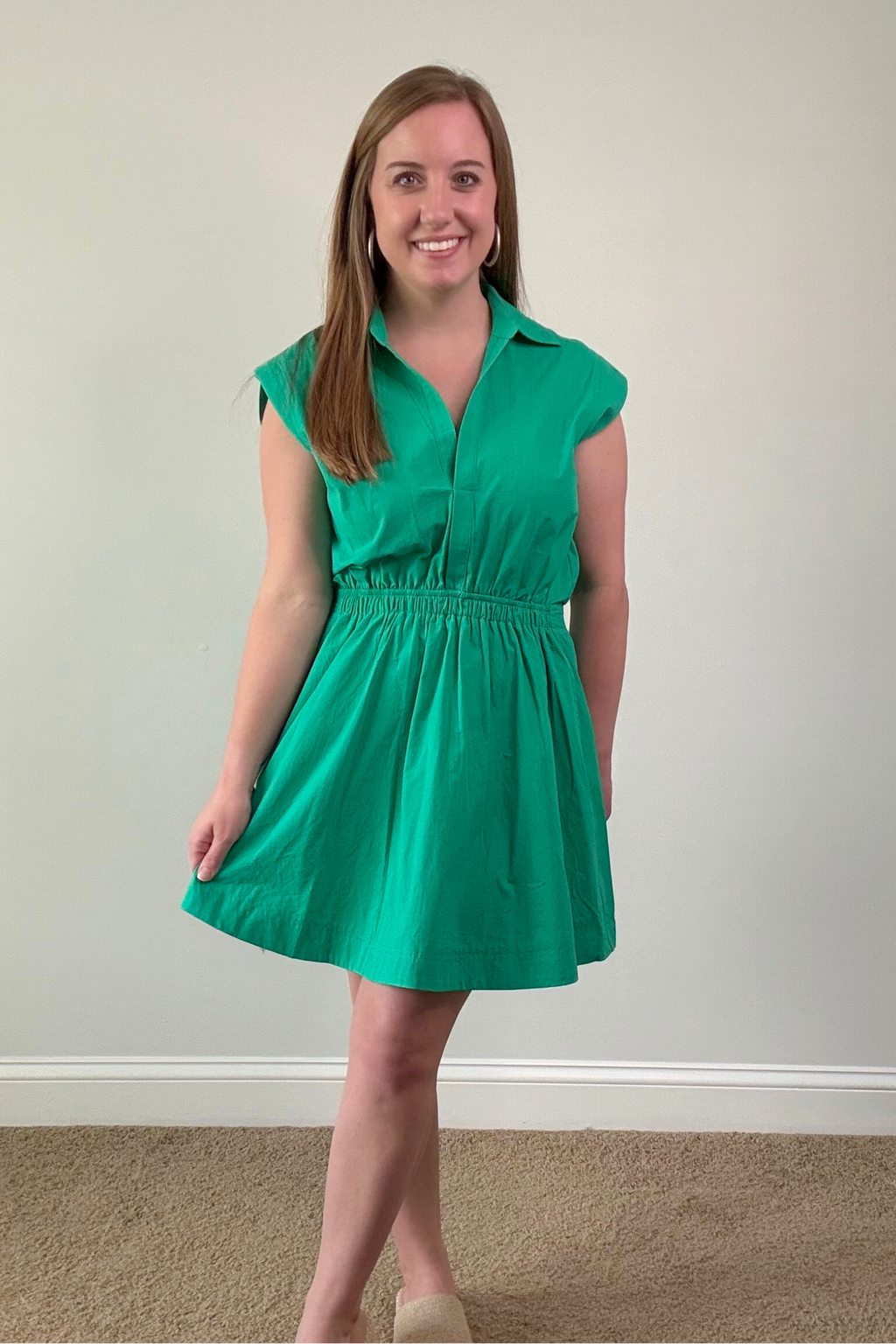 Woman wearing a green dress standing against a plain wall.