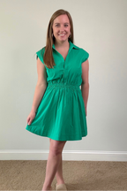 Woman wearing a green dress standing against a plain wall.