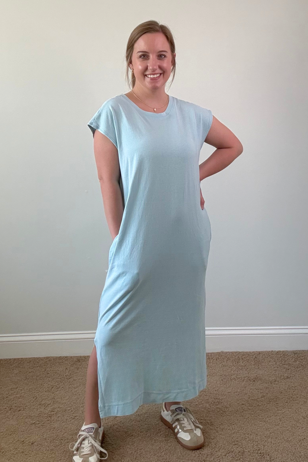 Woman wearing a light blue dress standing against a plain wall.