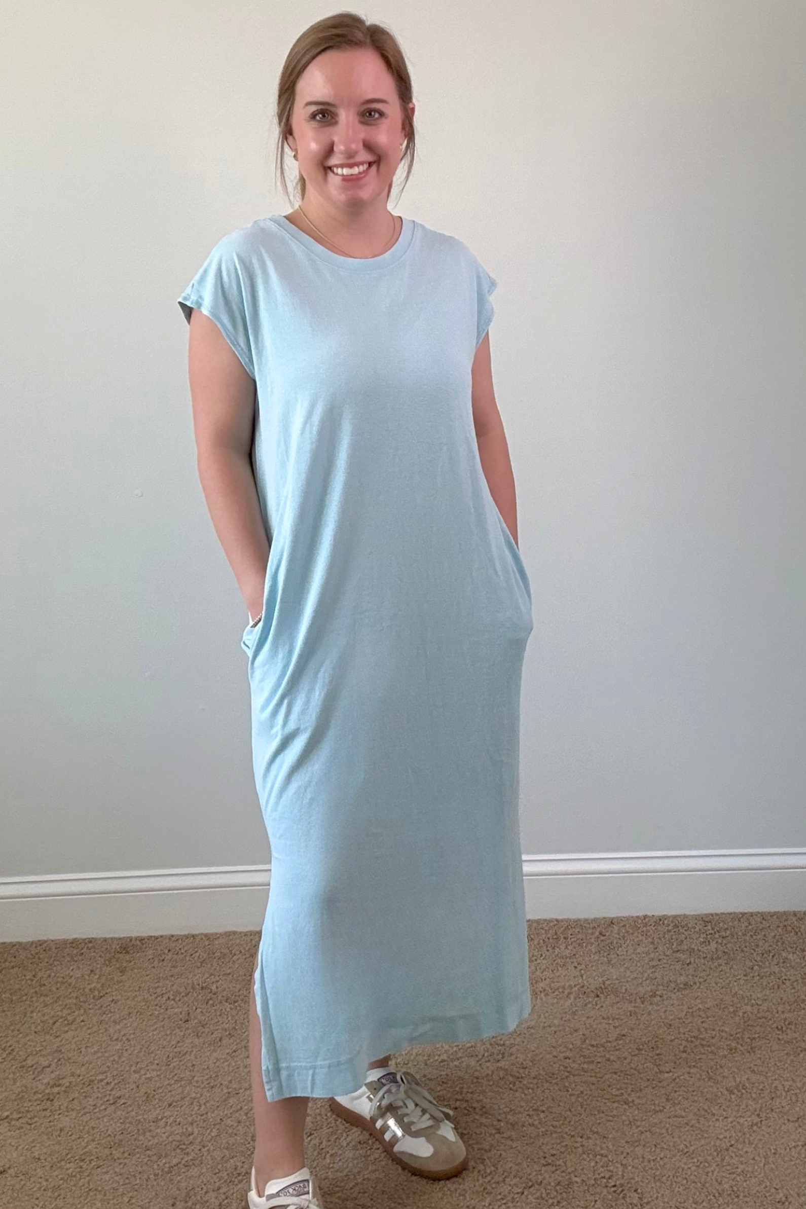 Woman wearing a light blue dress standing against a plain wall.