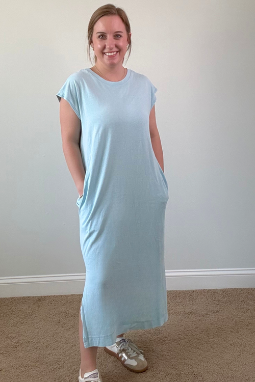 Woman wearing a light blue dress standing against a plain wall.