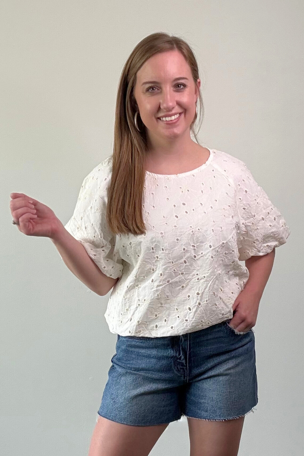 Woman wearing a white blouse with short sleeves and blue shorts on a plain background