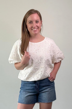 Woman wearing a white blouse and denim shorts against a plain background