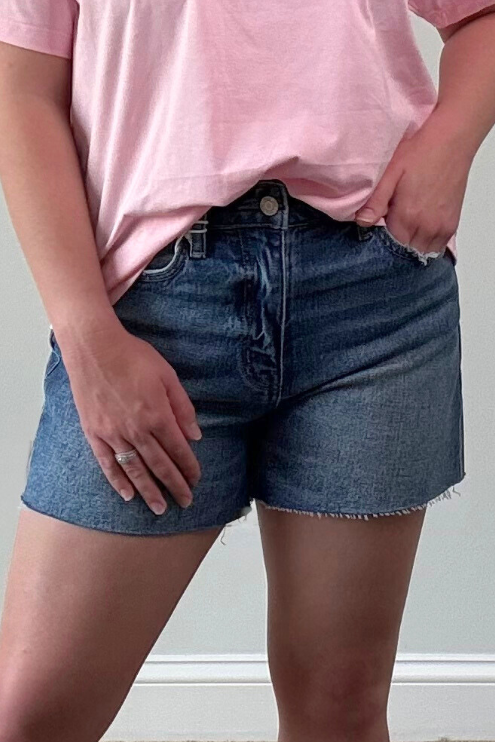 Person wearing a pink t-shirt and blue denim shorts against a neutral background