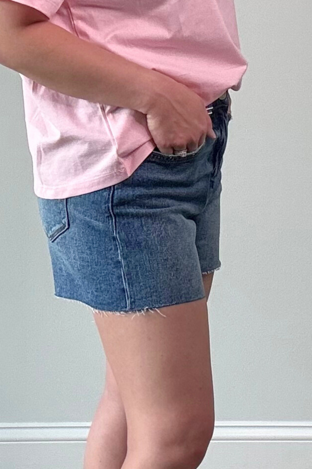 Person wearing a pink shirt and blue denim shorts against a plain background
