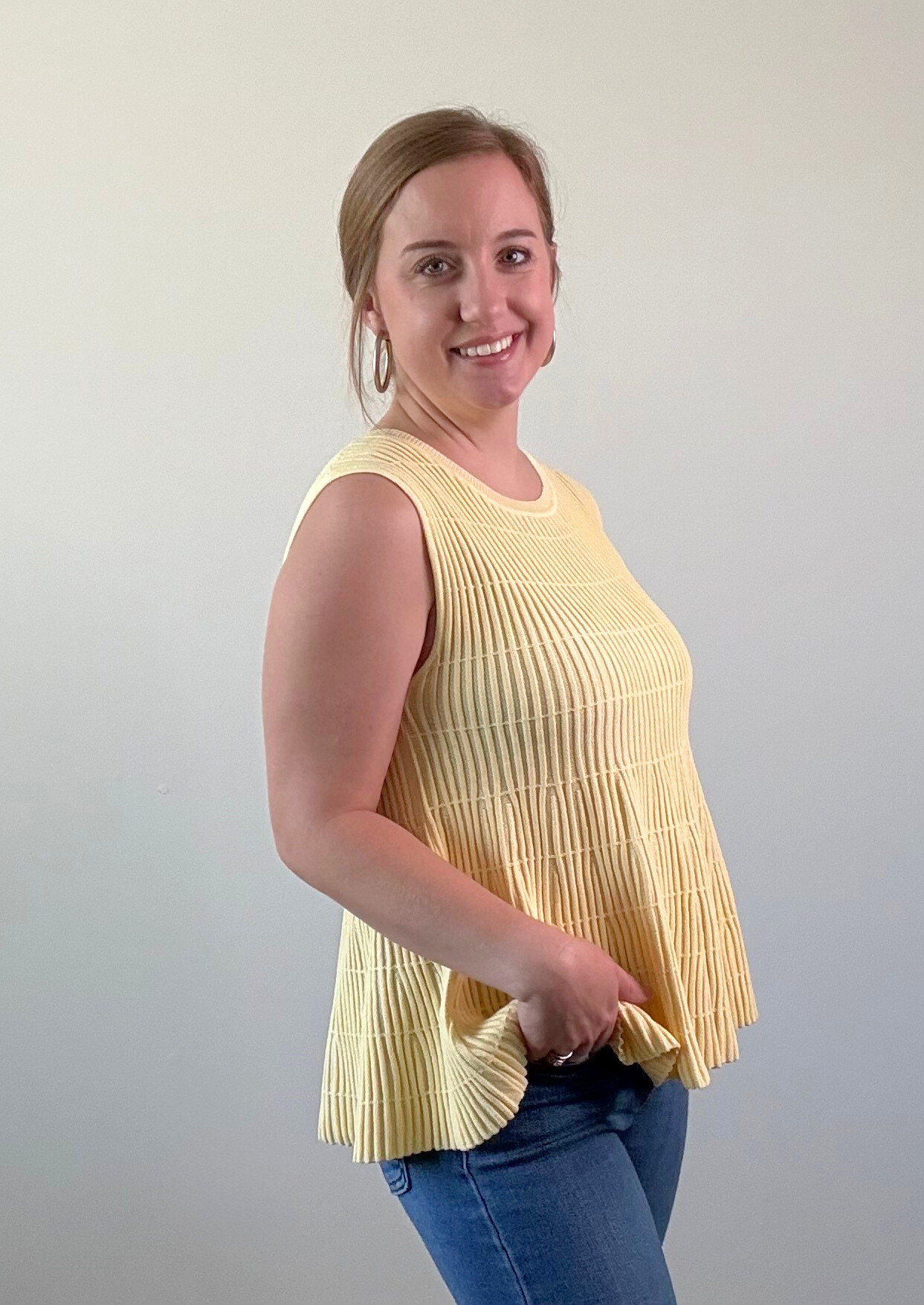 Woman wearing a yellow pleated top and blue jeans against a plain background