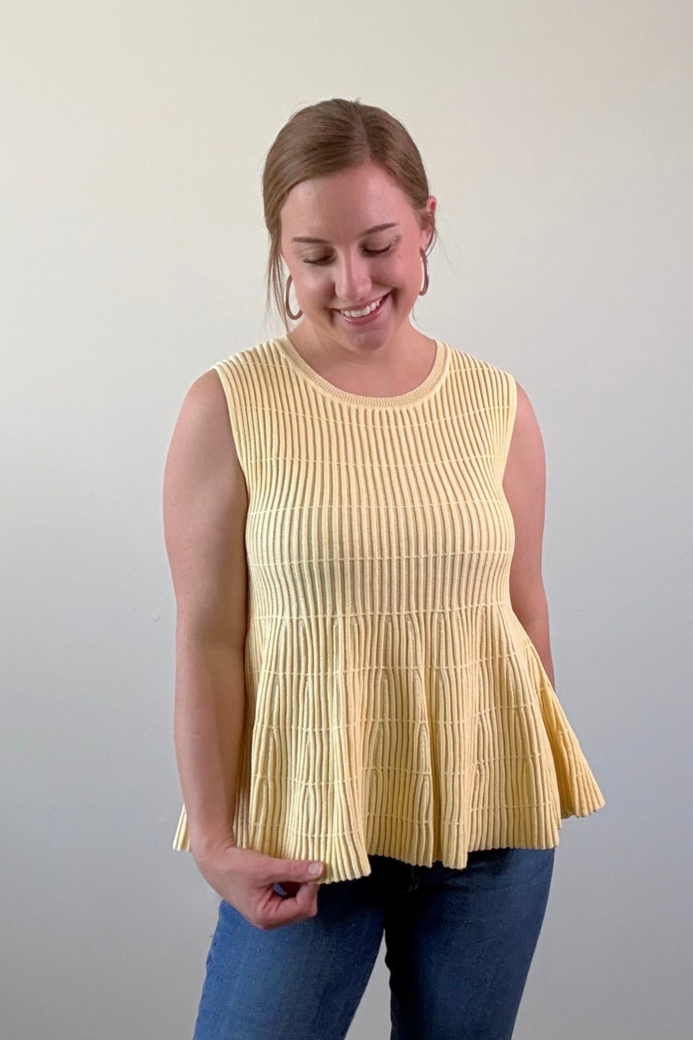 Woman wearing a yellow pleated top against a plain background