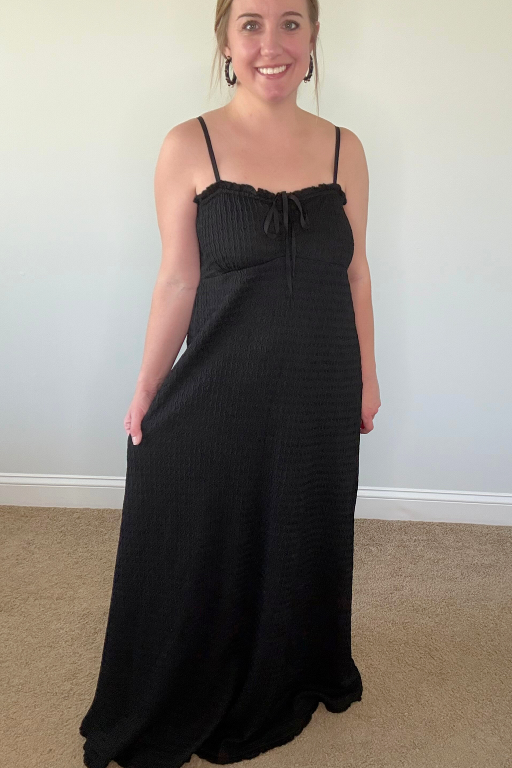 Woman wearing a black dress standing against a plain wall.
