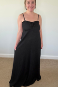 Woman wearing a black dress standing against a plain wall.