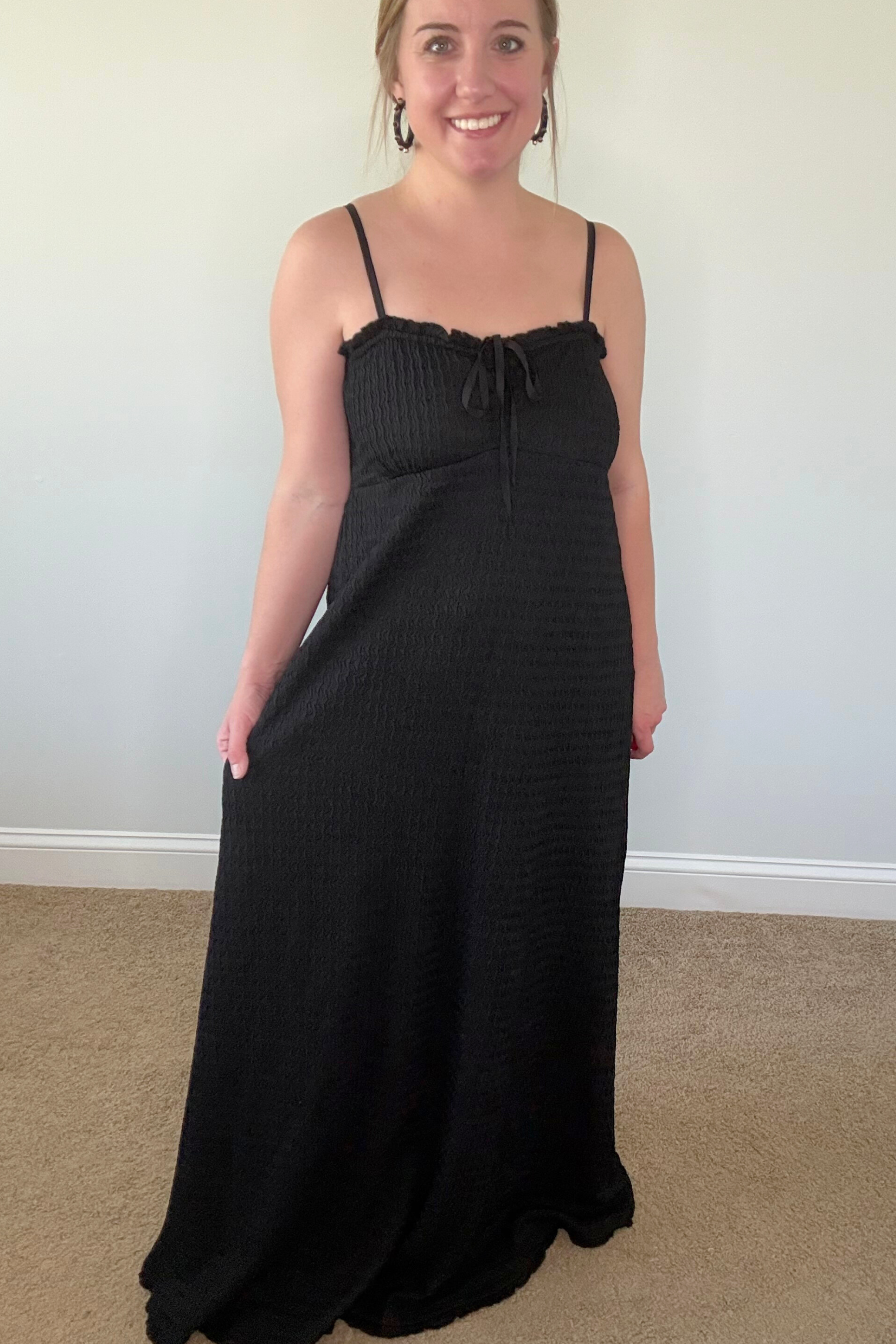 Woman wearing a black dress standing against a plain wall.
