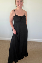 Woman wearing a black dress standing against a plain wall.