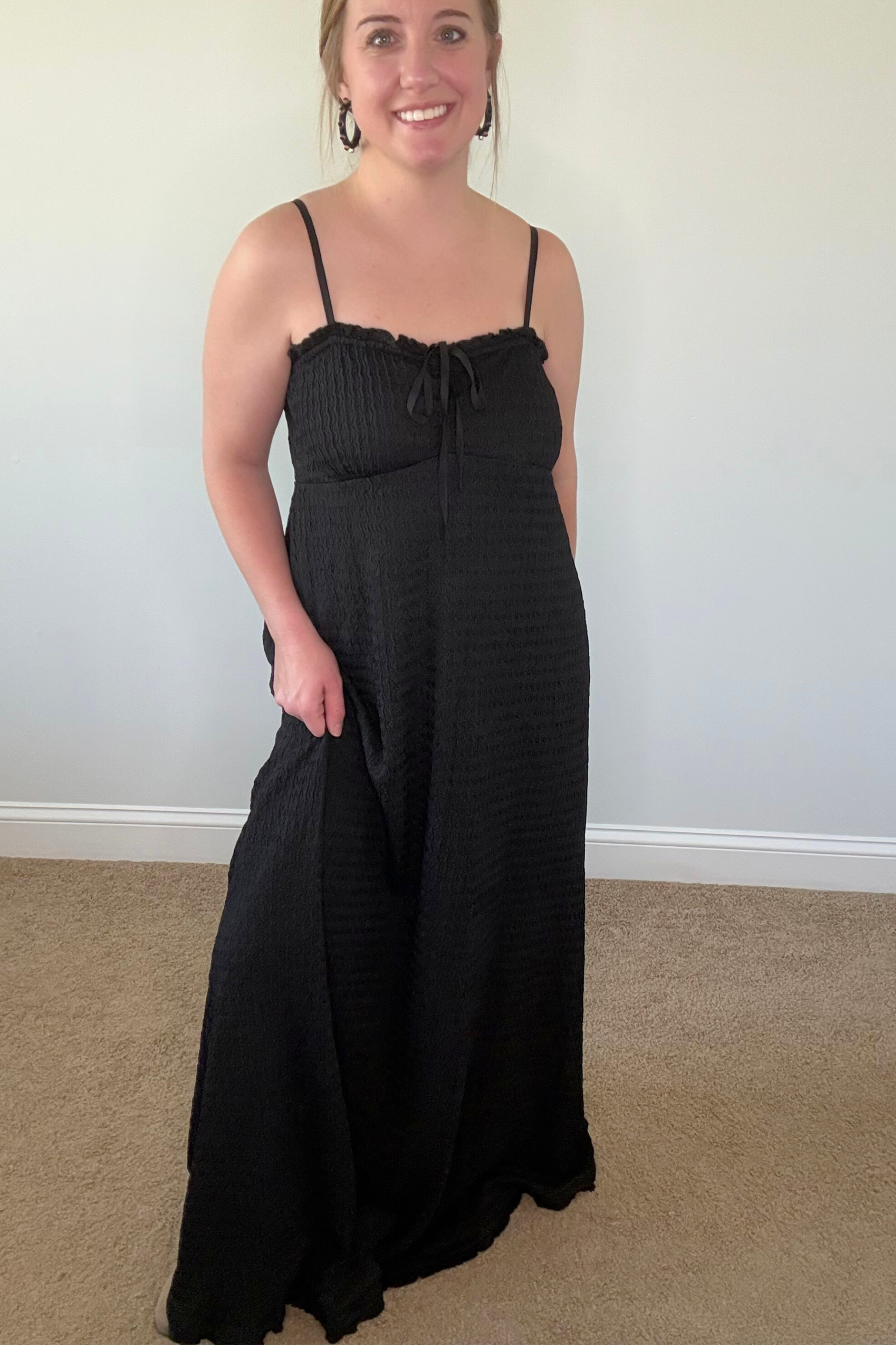 Woman wearing a black dress standing against a plain wall.