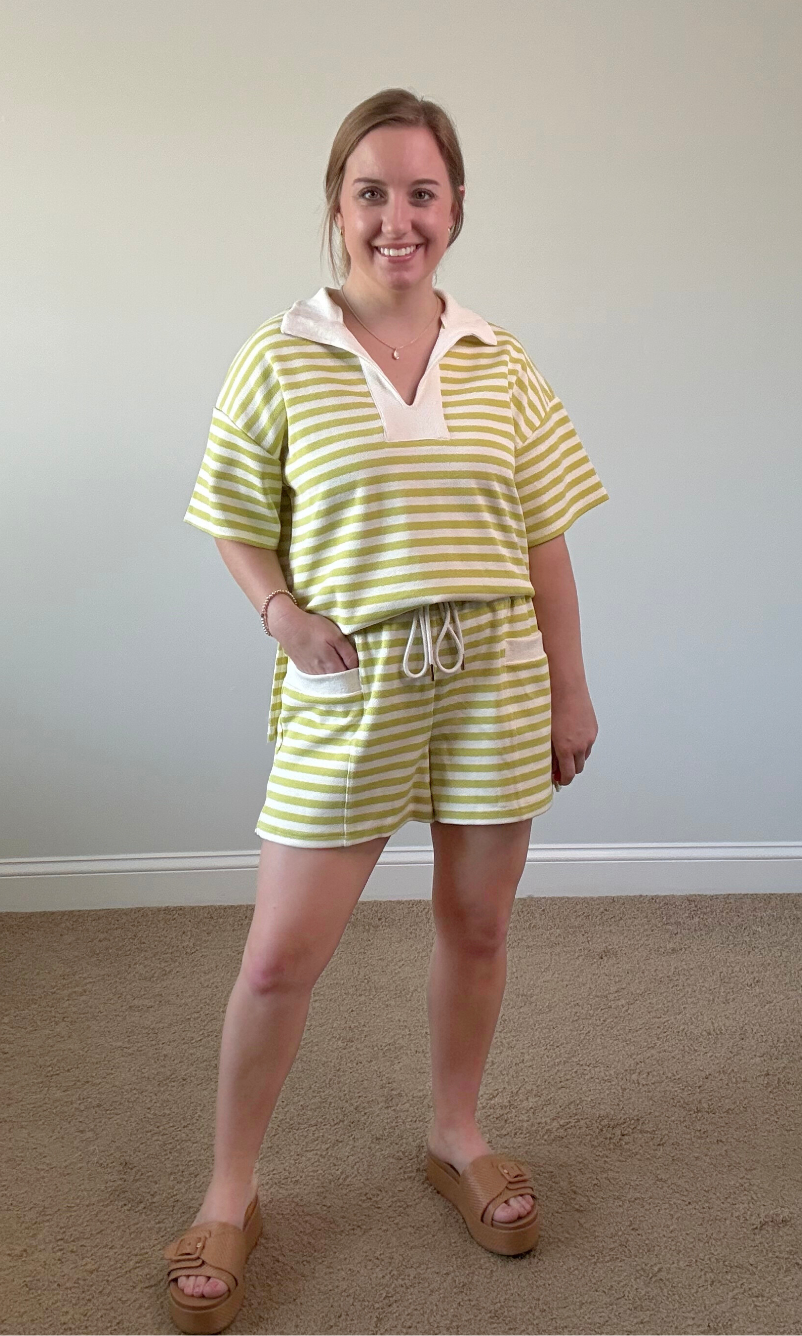 Woman wearing a yellow and white striped outfit standing against a plain wall.