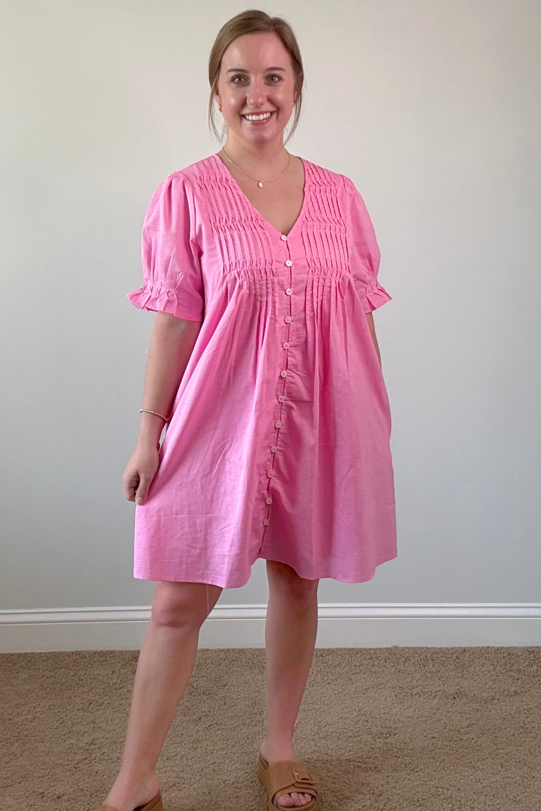 Woman wearing a pink dress standing against a plain wall.