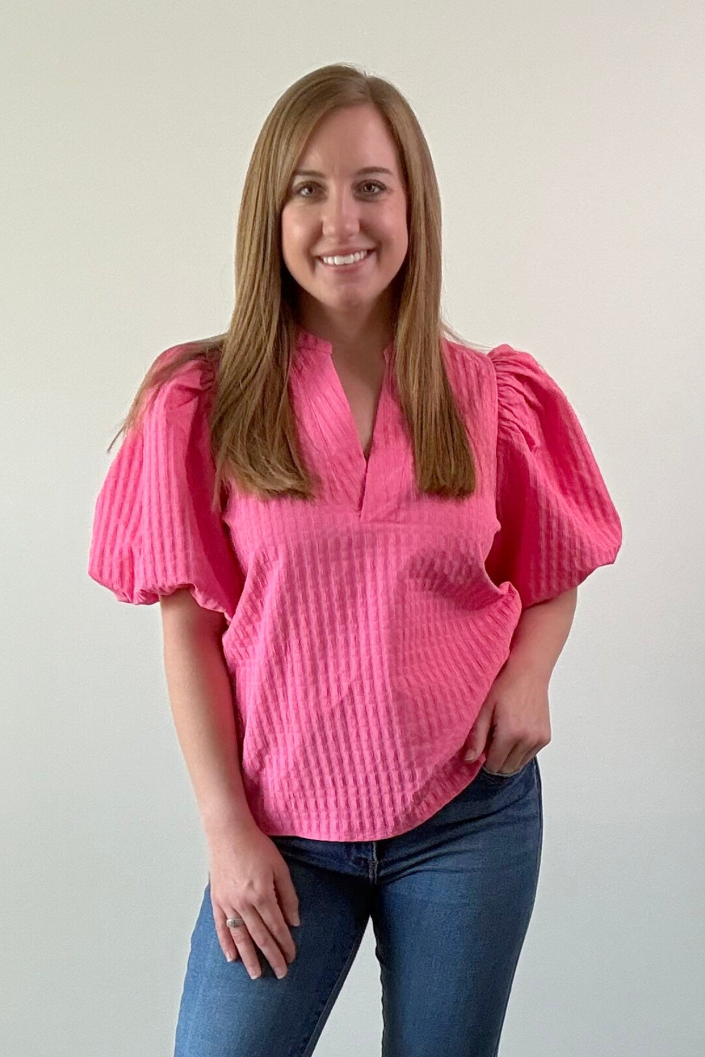 Woman wearing a pink textured blouse and blue jeans against a plain background