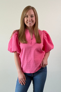 Woman wearing a pink textured blouse and blue jeans against a plain background